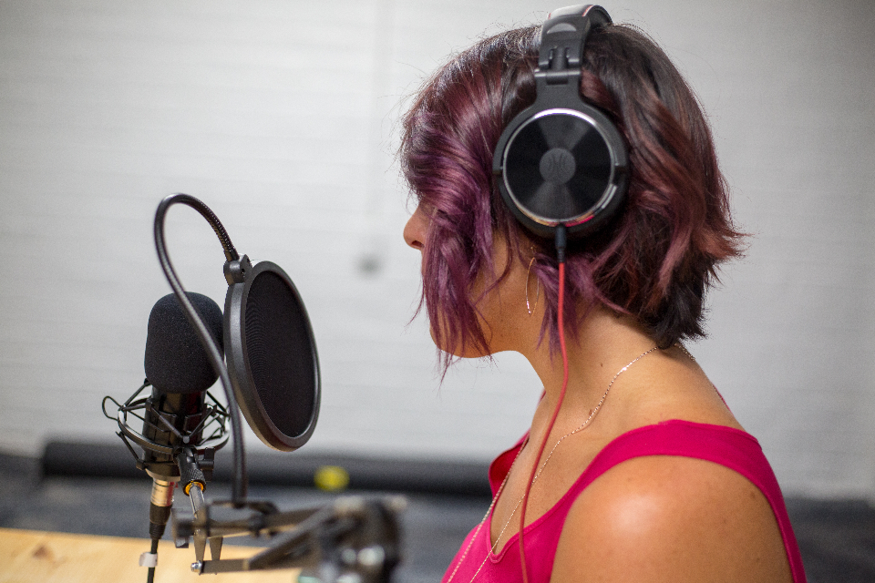 Kvinde med hovedtelefoner ved mikrofon, optager podcast i studie